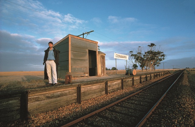 Man stands at a train station named Coonawarra with blue sky and red earth