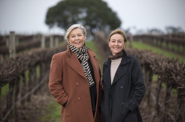 two women stand in a vineyard